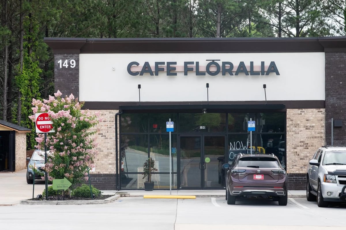 Exterior of Cafe Floralia Canton storefront with brick facade, CAFE FLORALIA signage, large windows, and address 149, surrounded by parked cars and landscaping